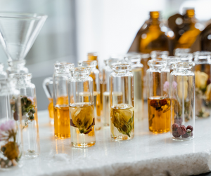 Glass vials filled with botanical essential oils and dried flowers, showcasing the natural ingredients used in handmade perfume blends with essential oil top, middle, and base notes.