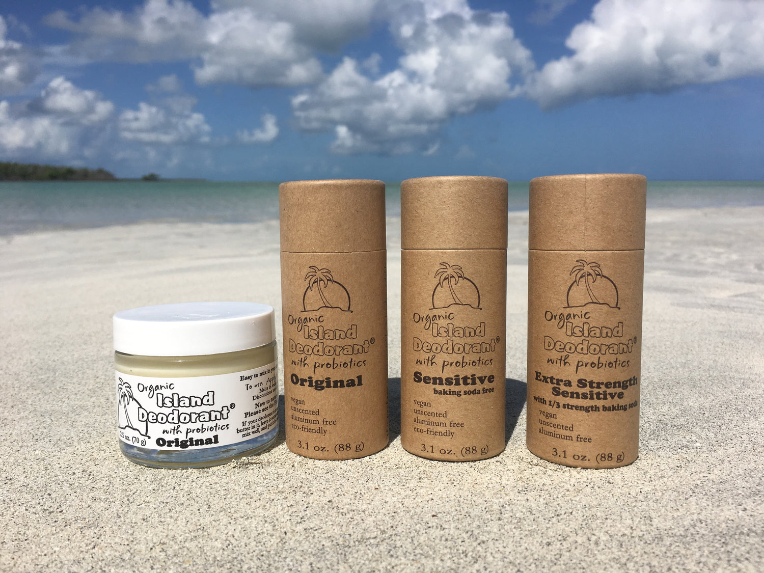 eco friendly vegan deodorant lineup on a tropical beach — Island Deodorant Original cream in a glass jar, plus Original, Sensitive, and Extra Strength Sensitive in compostable paperboard tubes