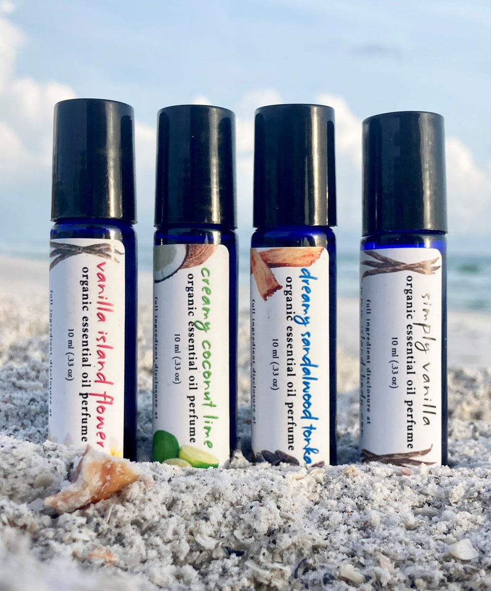 4 blue roller bottles of organic essential oil perfume, in the sand, in front of the ocean