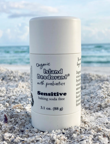 Baking Soda Free Deodorant, in white plastic twist up container, on the beach in front of the ocean