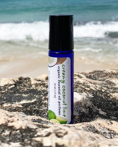 Coconut lime essential oil perfume roll-on bottle on a rocky beach with ocean waves in the background, representing a natural tropical scent.