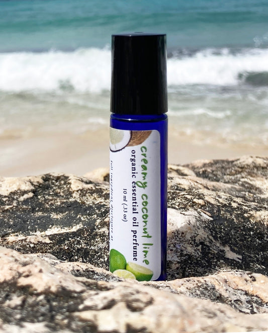 Coconut lime essential oil perfume roll-on bottle on a rocky beach with ocean waves in the background, representing a natural tropical scent.