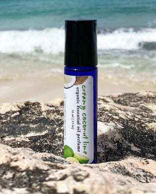A 10 ml blue glass roller bottle, filled with essential oil perfume, rests on a rock at the beach with the ocean waves in the background