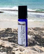 organic vanilla essential oil perfume roll-on bottle rests on a rock at the beach with the ocean waves in the background, 